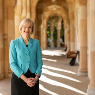 Woman in a blue jacket stands outside a shady sandstone building.